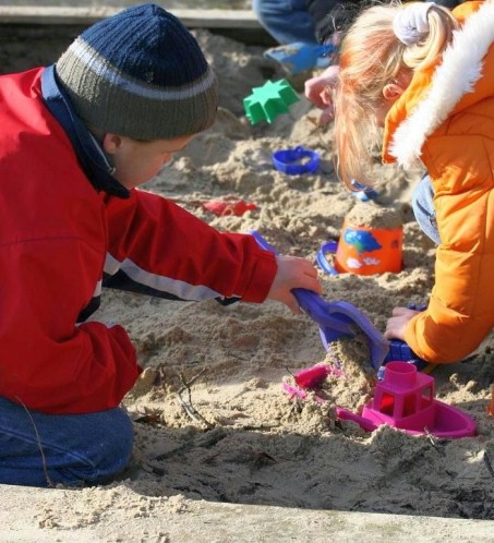 drei buntangezogene Kinder die mit Förmchen im Sandkasten spielen
