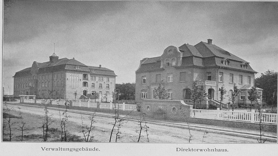Schwarz-Weiß-Foto: zwei große Häuser mit einer Straße im Vordergrund und Bäumen im Hintergrund