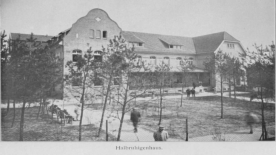 Schwarz-Weiß-Foto: dreistöckiges Haus mit einem Zaun rundherum und Bäumen im Vordergrund