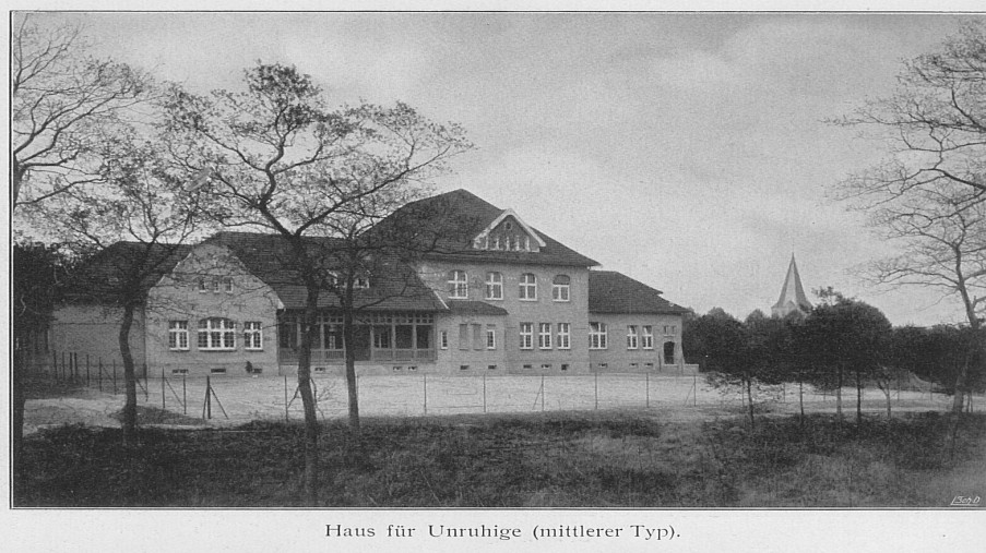 Schwarz-Weiß-Foto: Haus mit einem Zaun und Bäumen runderhum und im Hintergrund der Kirchturm