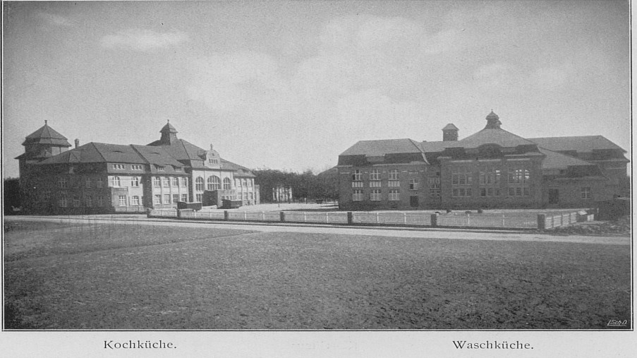 Schwarz-Weiß-Foto: zwei große Häuser mit einer Straße im Vordergrund und Bäumen im Hintergrund