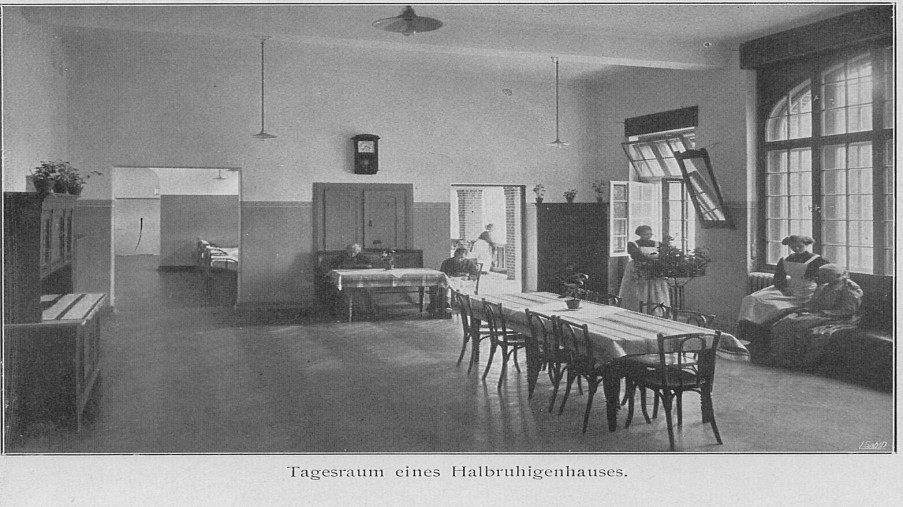 Schwarz-Weiß-Foto: großer Raum mit Fischgrätenparkett mit einem großen Tisch in der Mitte und Stühlen