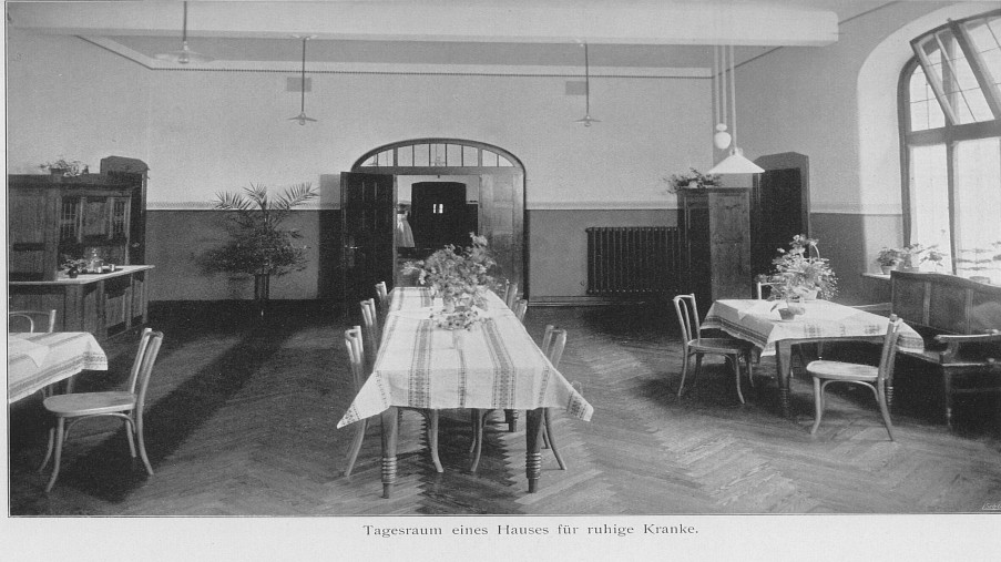 Schwarz-Weiß-Foto: großer Raum mit Fischgrätenparkett mit drei großen Tischen und Stühlen